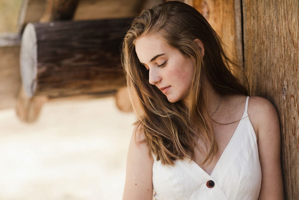 Woman in white dress leaning on wooden wall.