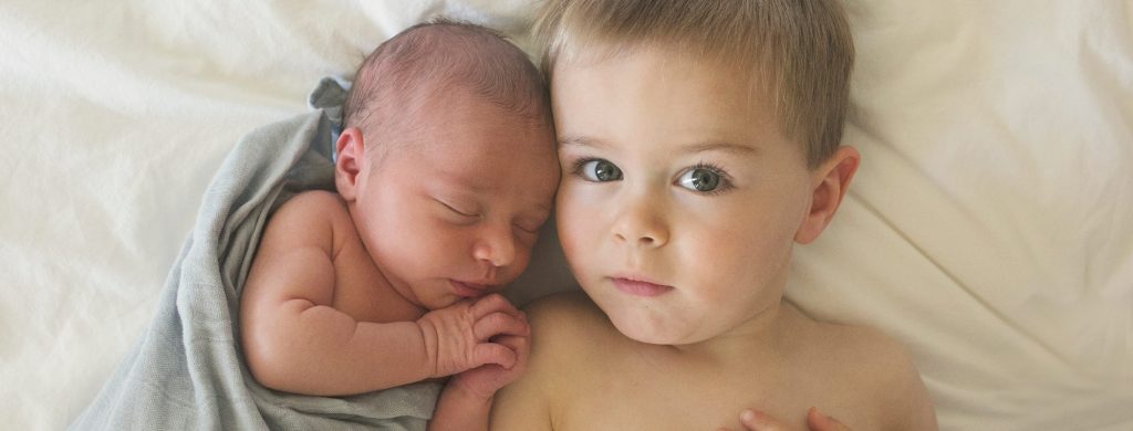 Toddler cuddling newborn baby on bed