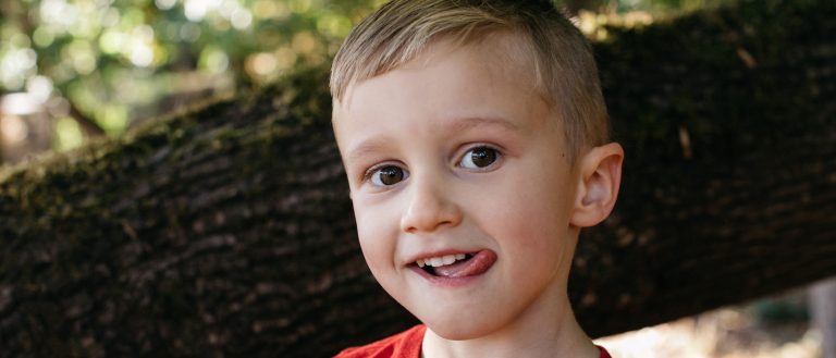 Smiling child outdoors, tongue out, playful expression.