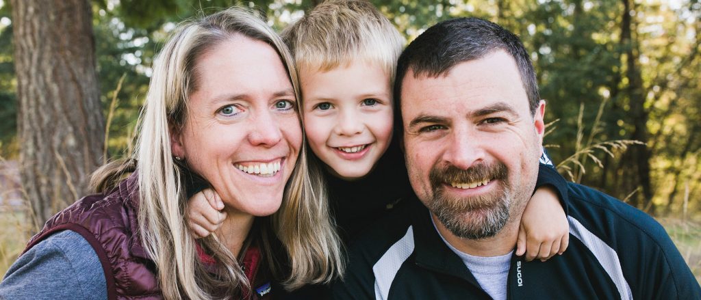 Smiling family outdoors in a forest setting.