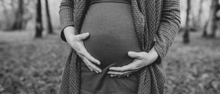 Pregnant belly with hands in nature.