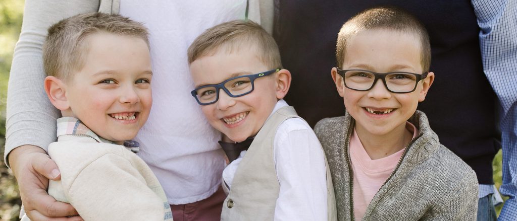 Three smiling kids with glasses hugging each other.