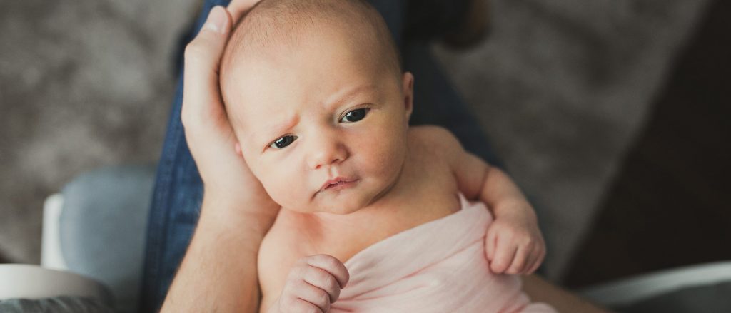 Newborn baby held in an adult's hand.