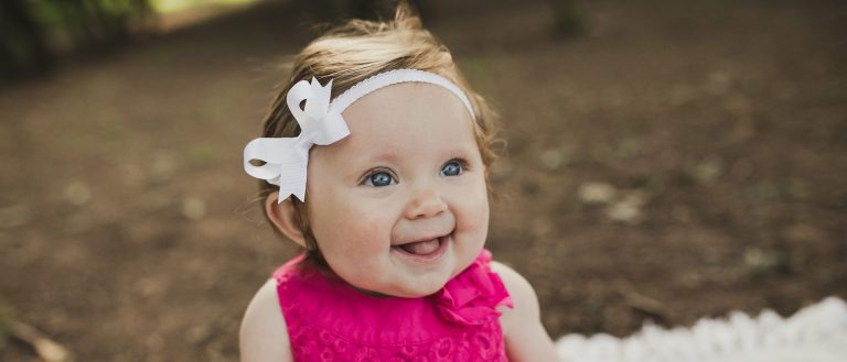 Smiling baby with bow in outdoor setting