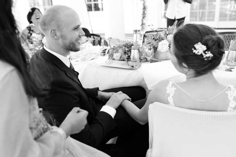 This over-the-shoulder photo catches the loving gaze of a groom as he sits at a wedding table with his new bride.