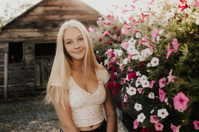 Sunlight warns the gentle smile and flaxen hair of a young woman in a country setting.