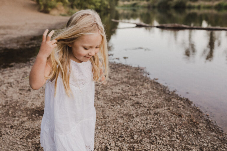 A five year old girl pulls a lock of blond hair away from her eyes as she joyfully explore the riverbank.