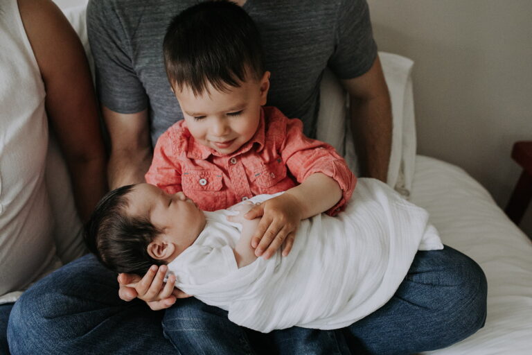 Toddler holding newborn baby, family bonding moment.