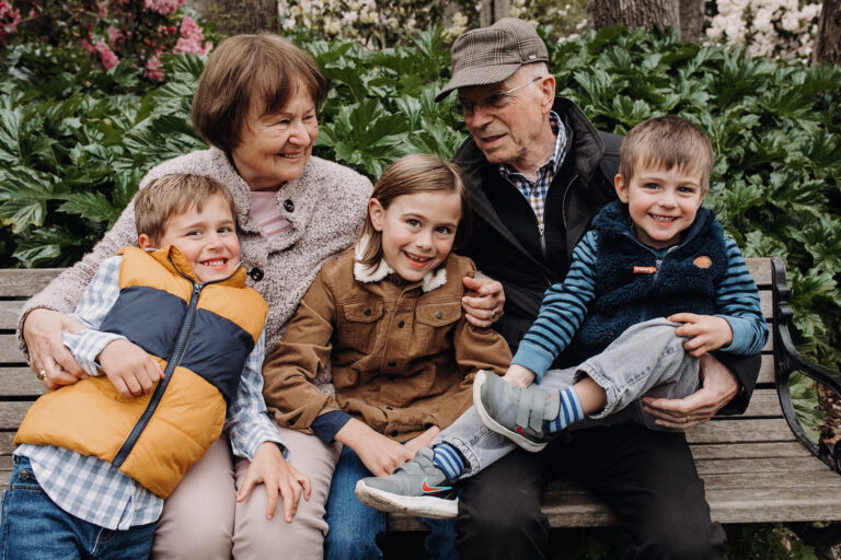 Two grandparents smile and laugh together, each with a smiling grandson tucked under each arm.