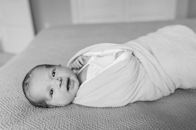 Newborn baby wrapped in blanket, black and white photo.