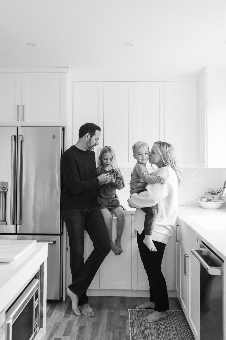 A candid black and white shot of a young couple and their two children interacting in the kitchen.