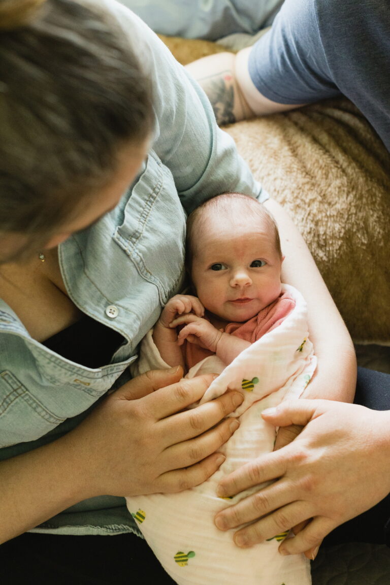An overhead shot shows a newborn's tentative grin as she's lovely cradled by the arms of her parents.