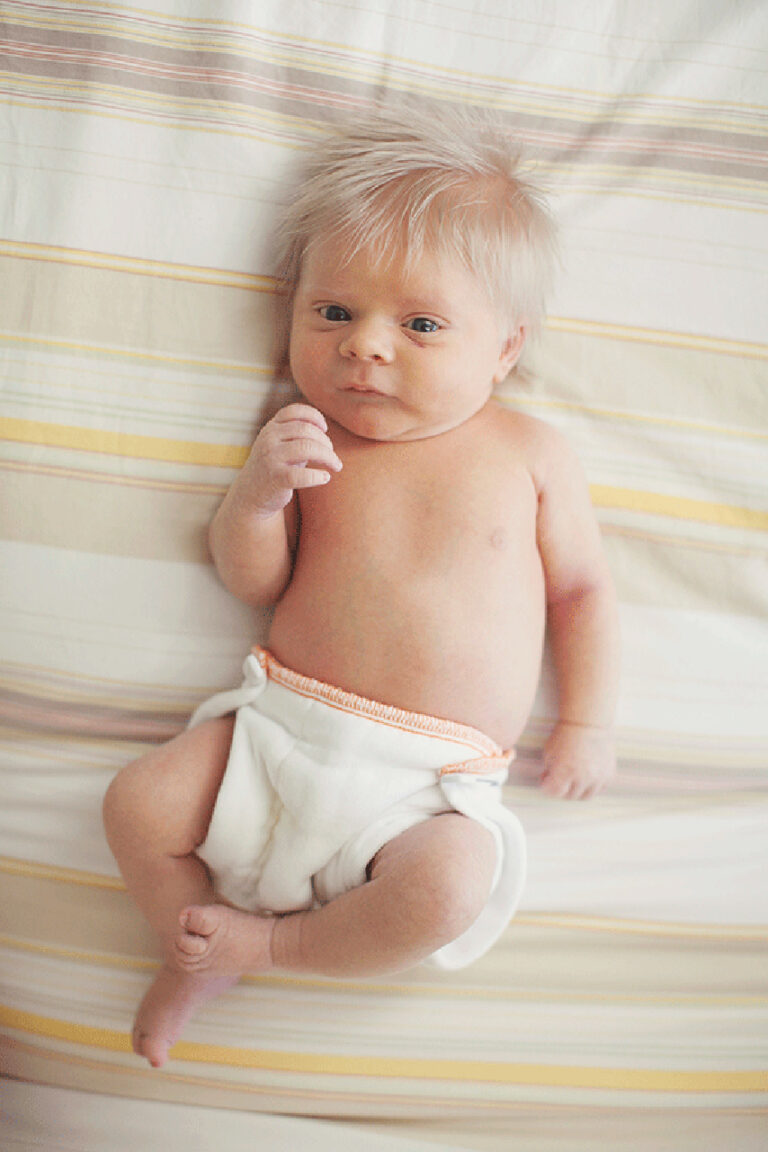 Newborn baby lying on striped bed.