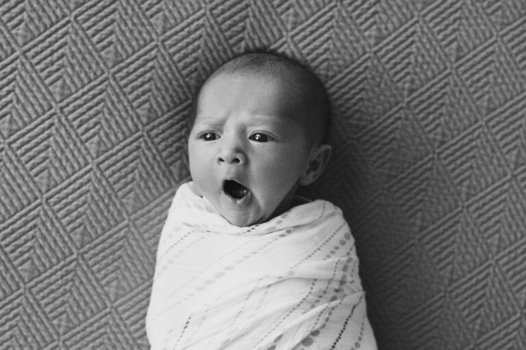 Yawning newborn wrapped in a blanket.