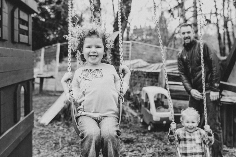 Children swinging with adult supervision outdoors.