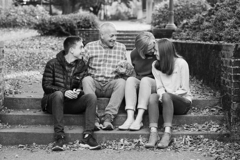 Family sitting on outdoor steps with dog, autumn leaves