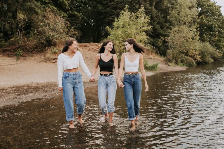 Three women joyfully walking hand in hand through shallow water, enjoying a sunny day together.