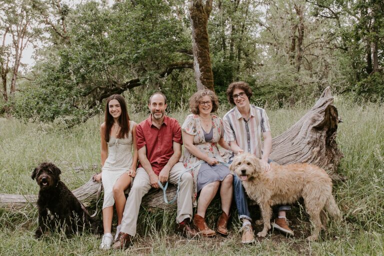 Family with two dogs on fallen tree in forest.