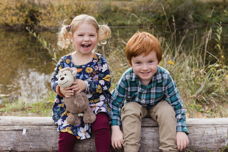 Laughing children sitting on a log by a pond
