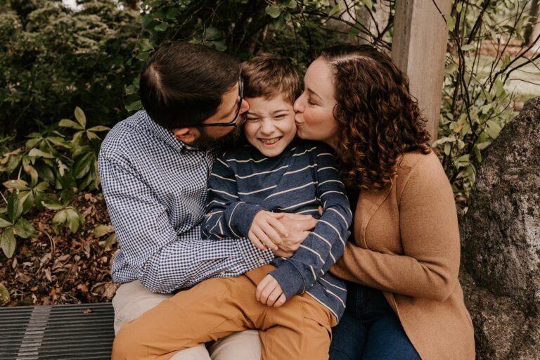 Family cuddling their smiling child outdoors.