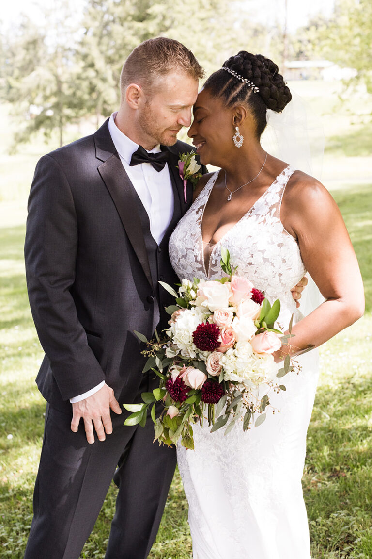 Bride and groom embracing in sunny outdoor setting.