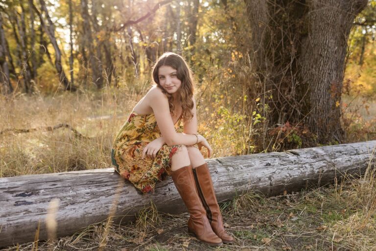 A young woman with a bright smile sits on a log, surrounded by lush greenery in a serene forest setting.
