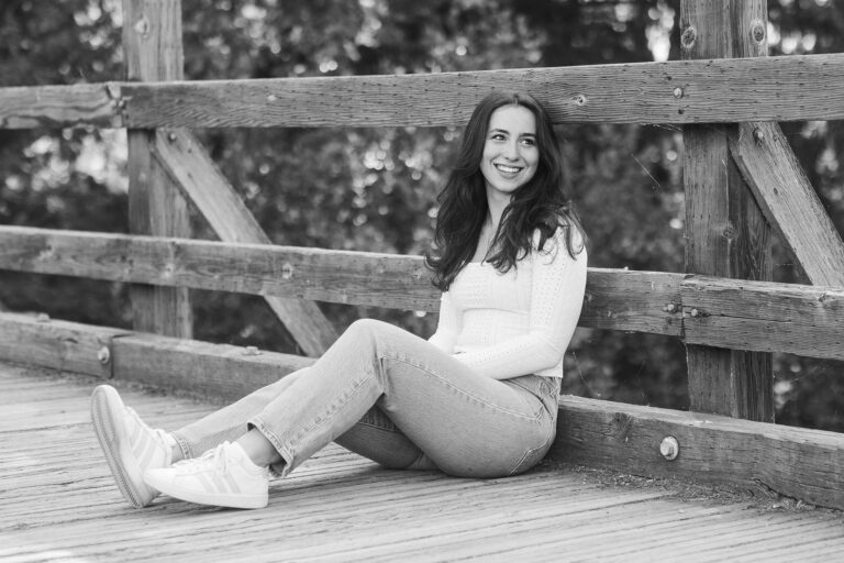 A girl sits on a bridge, captured in a serene black and white photograph, evoking a sense of calm and reflection.