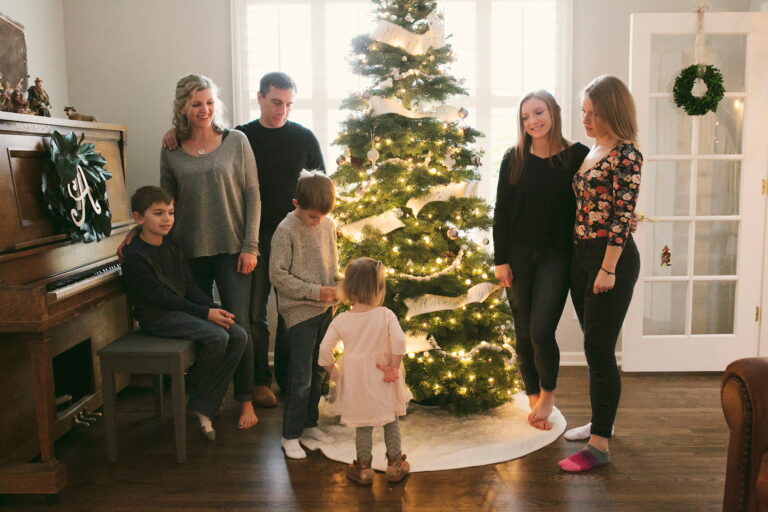 Family gathered around decorated Christmas tree indoors.