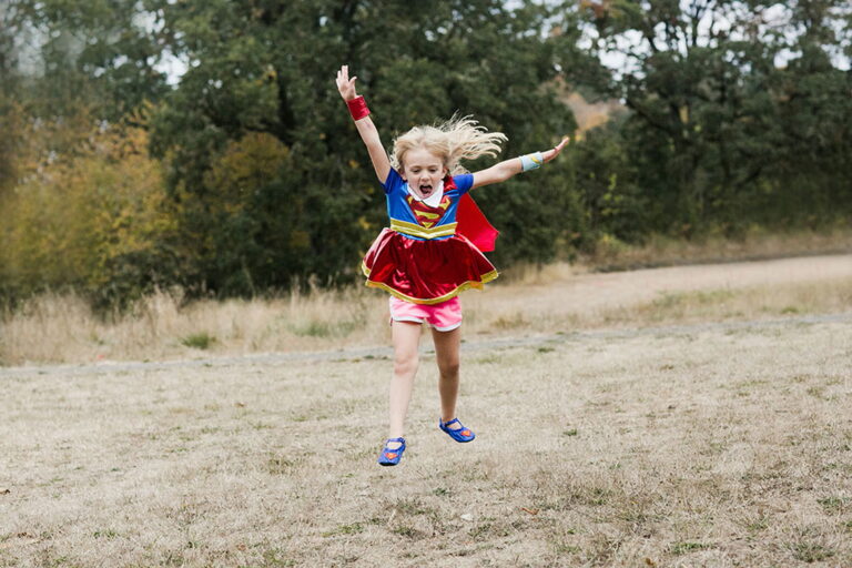 Child in superhero costume jumping outdoors