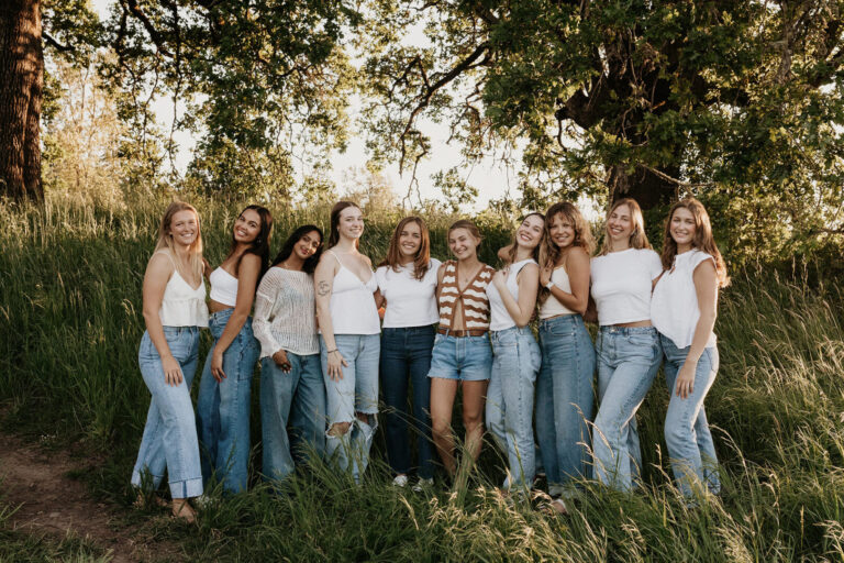 A group of high school seniors in jeans smiling and posing together for a photo outdoors.